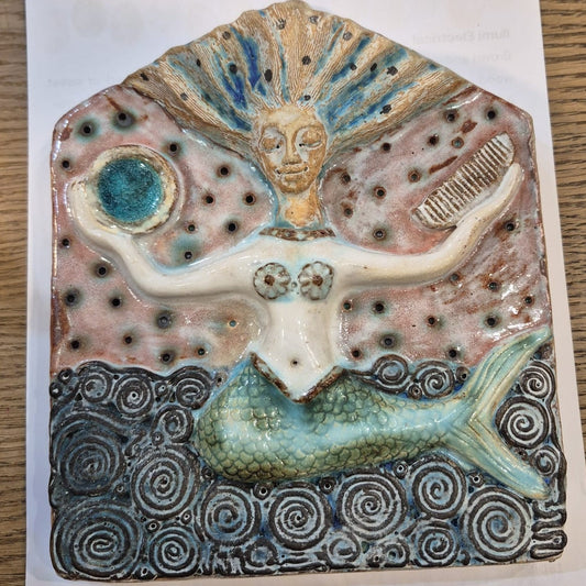 Ceramic artwork of a mermaid with shell-like head on a white background
